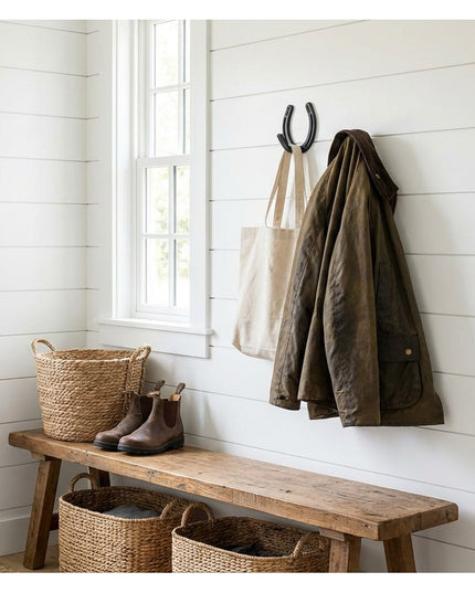 Black metal horseshoe wall hook by Industrial Farm Co mounted on white shiplap wall holding olive jacket and canvas tote b...
