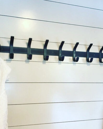 Black metal Christopher Double Hook Coat Rack by Industrial Farm Co mounted on white shiplap wall with baseball cap and wh...