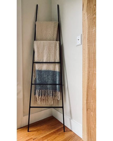 Black metal tapered farmhouse ladder by Industrial Farm Co displaying cream and blue textured blankets in corner against w...