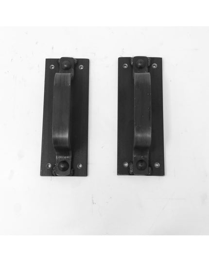 Two black metal Corning Handle door pulls by Industrial Farm Co with rectangular mounting plates and curved grip handles a...