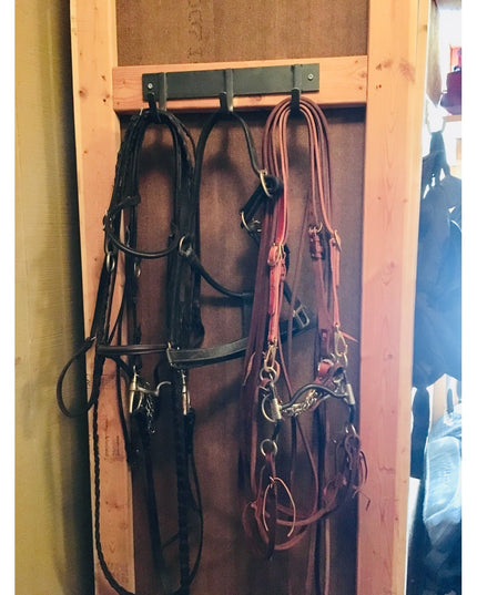 Industrial Farm Co Camillus Style black metal coat rack mounted on wood frame holding horse bridles and leather tack equip...