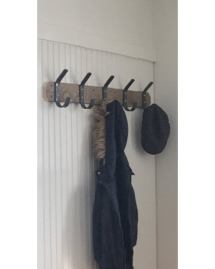 Rustic wood and black metal coat rack with 5 double hooks mounted on white beadboard wall, holding navy jacket and black h...
