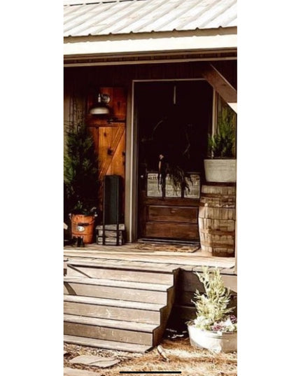 The Toby Firewood Holder by Industrial Farm Co in black metal positioned on rustic wooden porch steps near front door