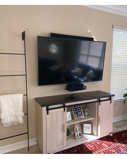 Black metal Brielle Top Mounted Blanket Ladder by Industrial Farm Co mounted on beige wall next to TV console with white t...