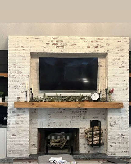 Black metal Toby Firewood Holder by Industrial Farm Co displayed next to white brick fireplace with wood mantel and built-...