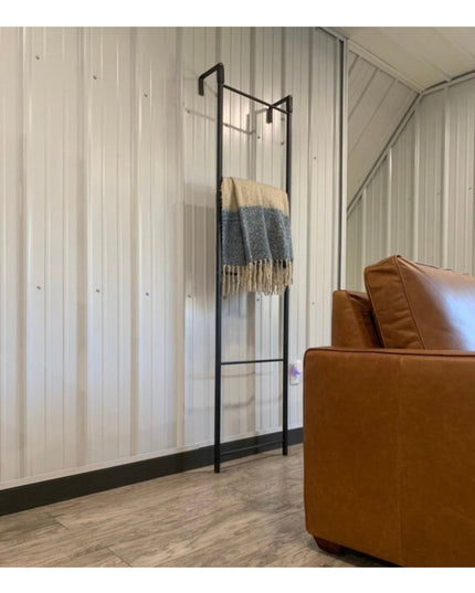Black metal Hal Standing Mounted Blanket Ladder by Industrial Farm Co with woven throws, displayed against white wood pane...