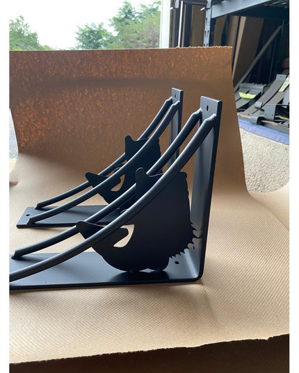 Black metal large mouth bass shaped shelf brackets by Industrial Farm Co displayed on cardboard packaging in workshop setting