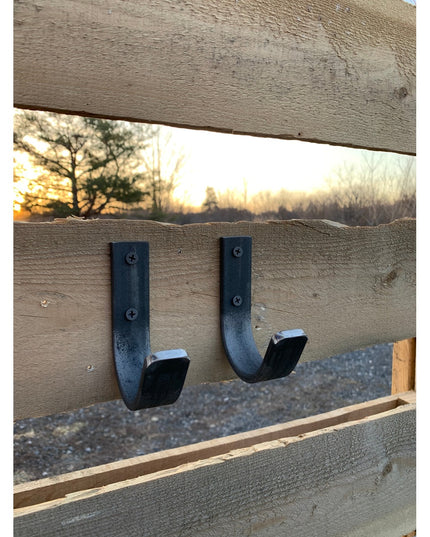 Two black metal Kinnley 1" Wide Wall Hooks by Industrial Farm Co mounted on rustic wood beam with sunset background