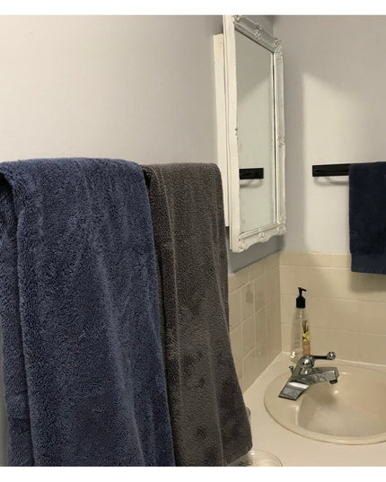 Black metal Oswego Modern Bathroom Towel Bar by Industrial Farm Co mounted on white bathroom wall with blue and gray towels
