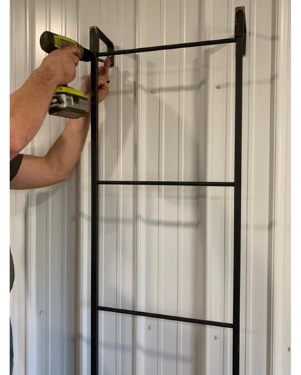 Person installing black metal Hal Standing Mounted Blanket Ladder against white wood paneled wall using cordless drill