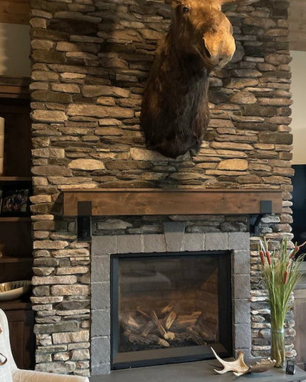 Rustic stone fireplace with wooden mantel supported by heavy duty steel brackets, featuring mounted moose head and built-i...
