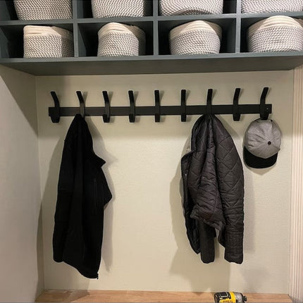 Black metal Christopher Double Hook Coat Rack by Industrial Farm Co mounted on white wall with baskets above, holding dark...