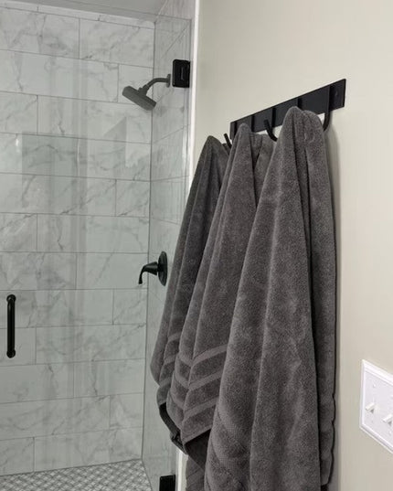 Black metal Camillus Style Coat Rack by Industrial Farm Co mounted on bathroom wall holding gray towels near marble shower