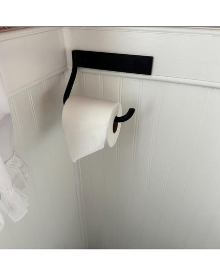 Black wrought iron Howlett Hill toilet paper holder mounted on white wainscoting wall with toilet paper roll installed
