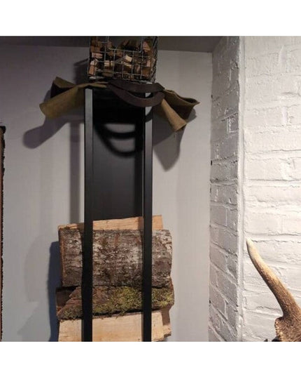 Industrial Farm Co Toby black metal firewood holder storing split logs against white brick wall with rustic jacket draped ...