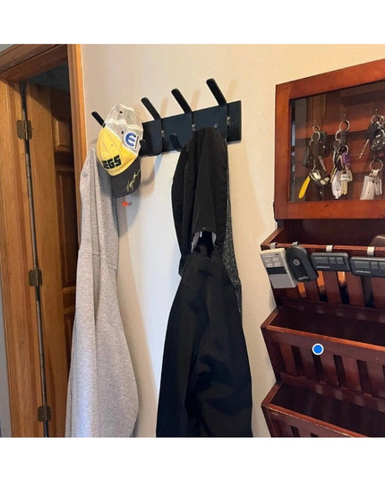 Black wall mounted metal coat rack with 5 hooks holding gray robe and baseball cap in entryway with wooden stairs and key ...