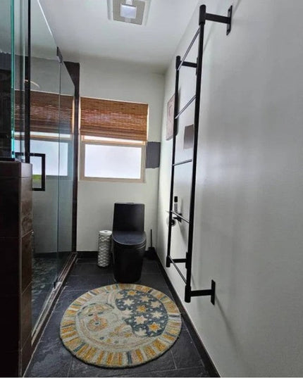 Black metal wall-mounted Ossit ladder by Industrial Farm Co installed in modern bathroom with glass shower and decorative ...