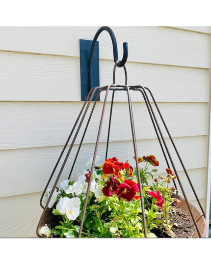 Black Gregory Shepherd Hook by Industrial Farm Co mounted on white siding, holding wire cage planter with colorful pansies...