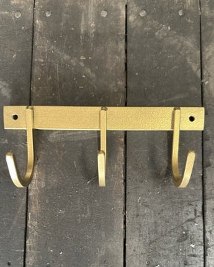 Rustic brass-colored metal key rack with three curved hooks mounted on weathered gray wooden planks background by Industri...