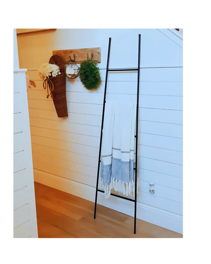 Black metal tapered farmhouse ladder by Industrial Farm Co leaning against white shiplap wall with blue striped towel