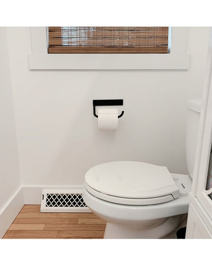 The Howlett Hill black metal toilet paper holder by Industrial Farm Co mounted on white bathroom wall with white toilet an...