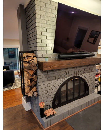 Black metal Toby Firewood Holder by Industrial Farm Co mounted on brick fireplace, holding stacked firewood logs