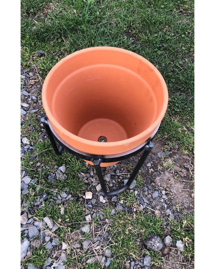 Industrial Farm Co Dorio Raised Planter in terracotta orange with black metal stand on grass and gravel ground