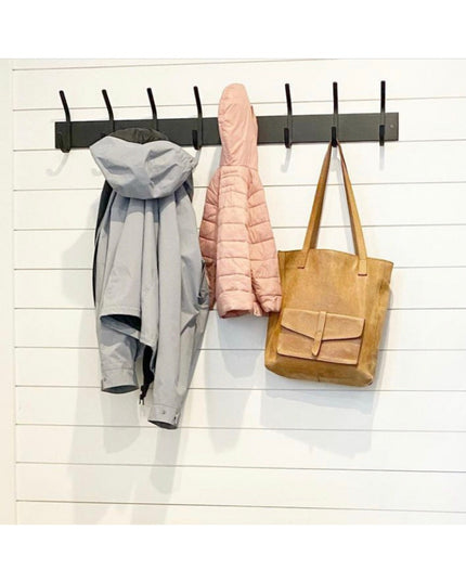 The Cooperstown Double Hook black metal coat rack mounted on white shiplap wall with gray jacket, pink puffer coat, and br...
