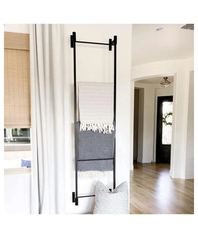 Black metal wall-mounted Ossit ladder by Industrial Farm Co displaying striped throw blankets in modern white living room ...