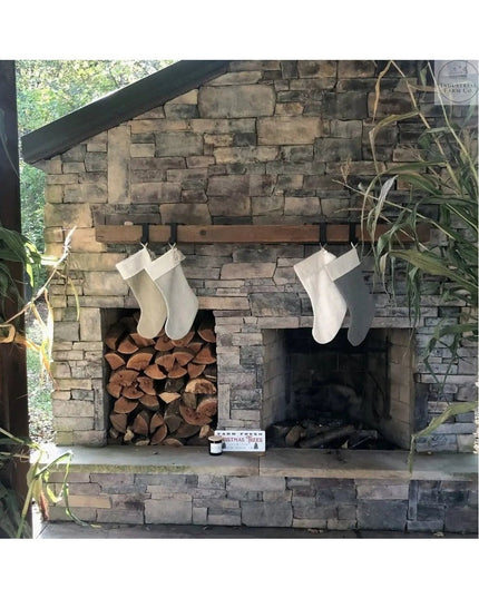 Black metal Annie Stocking Holders from Industrial Farm Co hanging four white Christmas stockings on rustic stone fireplac...