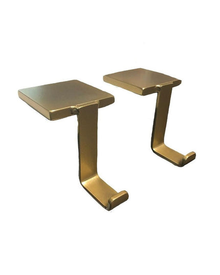 Two brass-colored metal Annie Stocking Holders by Industrial Farm Co with rectangular tops and curved hooks for hanging Ch...