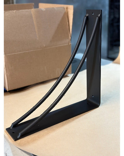 Black metal Sawmiller Shelf Bracket by Industrial Farm Co with angled support design on wooden surface with cardboard box