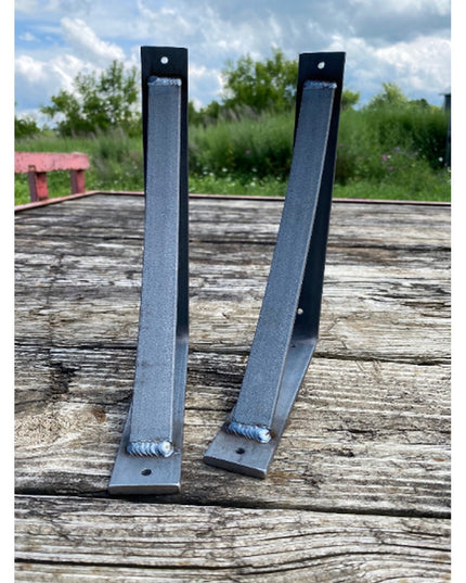 Two black metal Rey Bracket Supports by Industrial Farm Co positioned on weathered wood surface, showing angled steel cons...