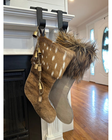 Black metal Annie Stocking Holder by Industrial Farm Co displaying two fur Christmas stockings with bells on white firepla...