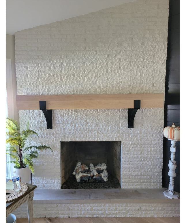 Black metal Seneca 3" farmhouse mantel brackets supporting natural wood beam on white painted brick fireplace by Industria...