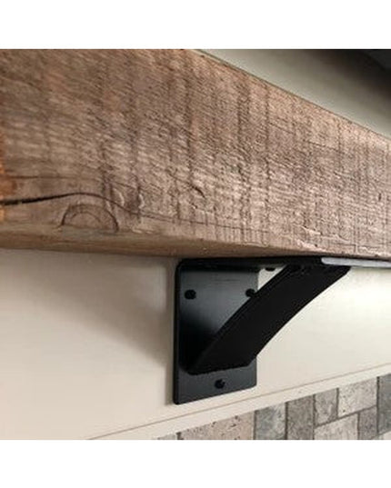 Black steel Albany 4-inch industrial shelf bracket with curved support bar mounted under rustic wood beam against brick ba...