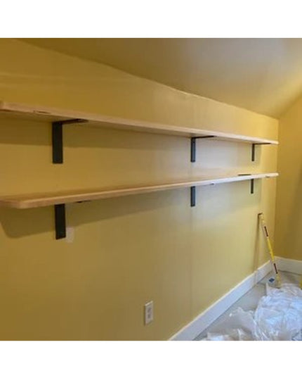 Black steel L-shaped shelf brackets supporting white wooden shelves mounted on yellow wall, showing Industrial Farm Co Owa...