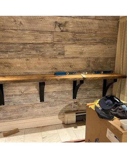Black metal Rochester desk support brackets mounted under wood shelf against rustic wood plank wall with level tool - Indu...