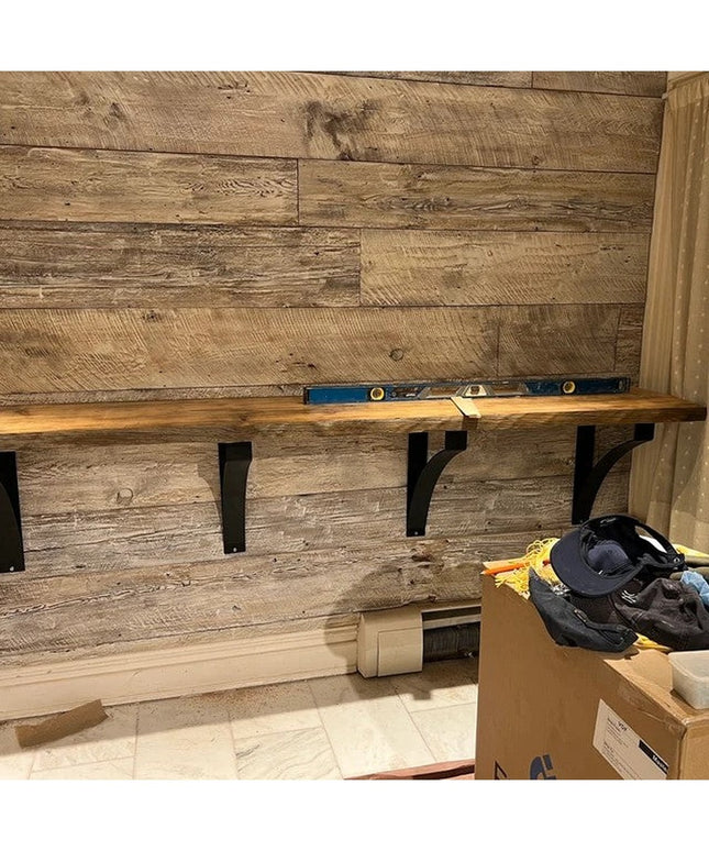 Black metal Rochester desk support brackets mounted under wood shelf against rustic wood plank wall with level tool - Indu...