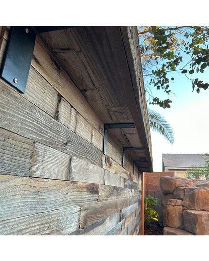 Heavy duty black steel L-shaped shelf brackets mounted under wooden deck overhang by Industrial Farm Co, showing 3-inch wi...