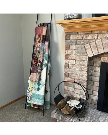 Black tapered farmhouse ladder from Industrial Farm Co displaying quilts beside brick fireplace with wood mantel
