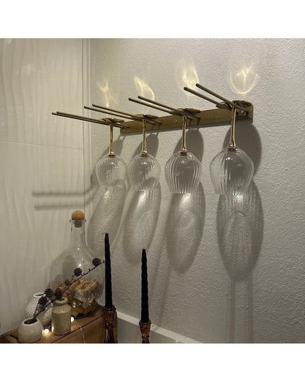 Wall-mounted bronze metal wine glass rack holding four clear wine glasses upside down, casting elegant shadows on textured...