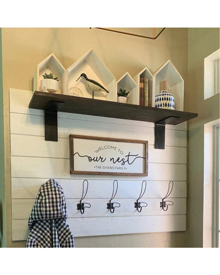 Black steel L-shaped shelf brackets supporting dark wood floating shelf with house-shaped decorative shelves above white s...