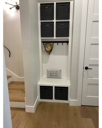 White built-in mudroom storage unit with black wicker baskets, coat hooks, bench seating and decorative pillow in modern f...