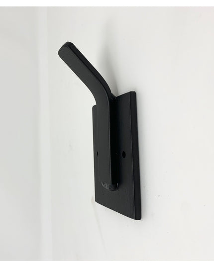 Black metal Tator Wall Mounted Hook by Industrial Farm Co mounted on white wall, featuring curved arm and rectangular back...