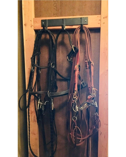 Industrial Farm Co Camillus Style black metal coat rack mounted on wooden frame holding horse bridles and leather tack equ...