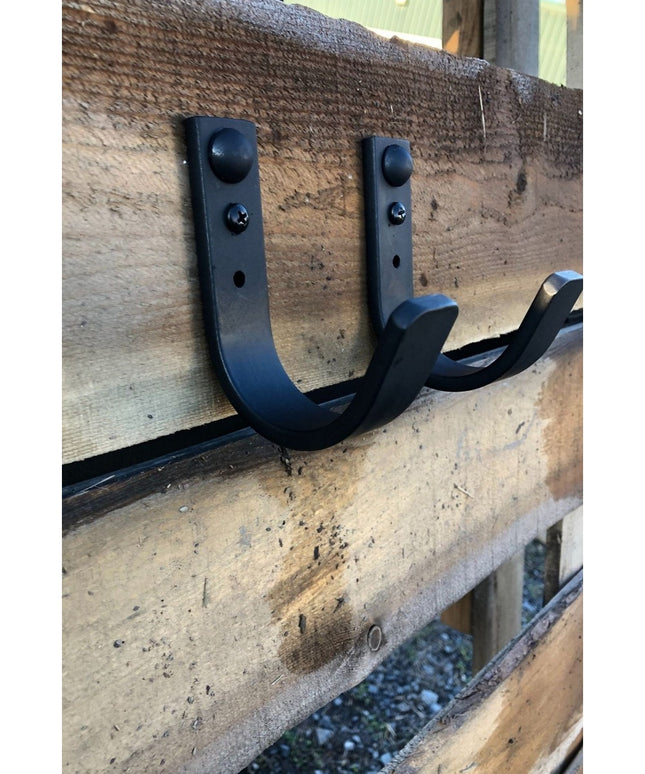 Black metal Westley 1" wide wall hooks by Industrial Farm Co mounted on rustic wooden beam, showing curved design and moun...