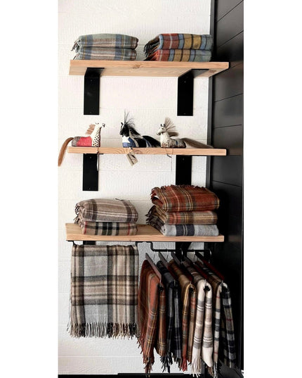 Black steel L-shaped shelf brackets supporting natural wood shelves displaying folded plaid blankets and decorative horses...