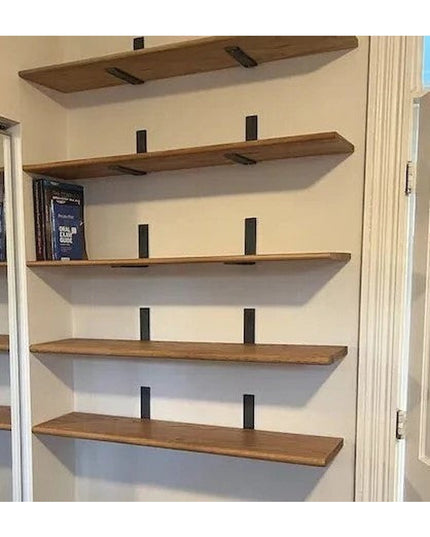 Black metal L-shaped shelf brackets supporting natural wood floating shelves mounted on white wall displaying books in hom...