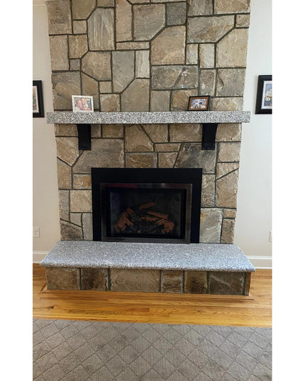 Stone fireplace with granite mantel supported by black Parish Style Bracket corbels from Industrial Farm Co, featuring nat...